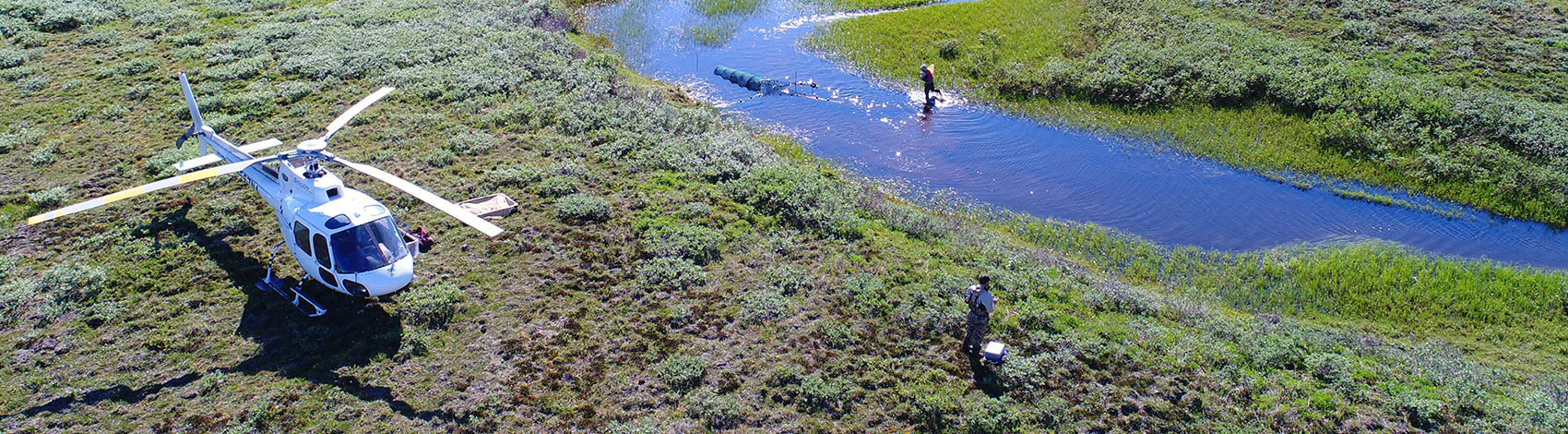 Aerial view of researchers at work by creek with landed helicopter.